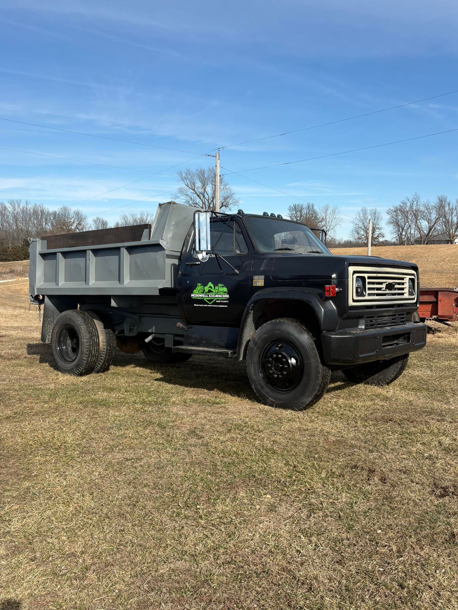 Black dump truck with gray bed parked on a grassy lot under a blue sky