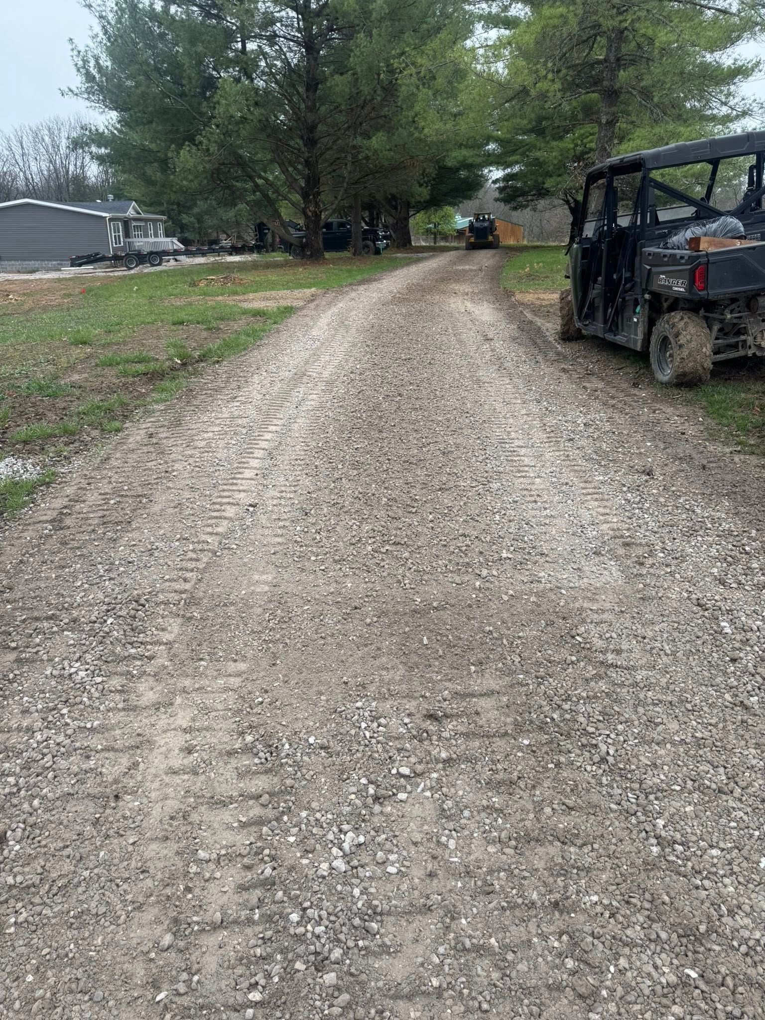Gravel driveway lined with trees, with a black utility vehicle parked on the right.