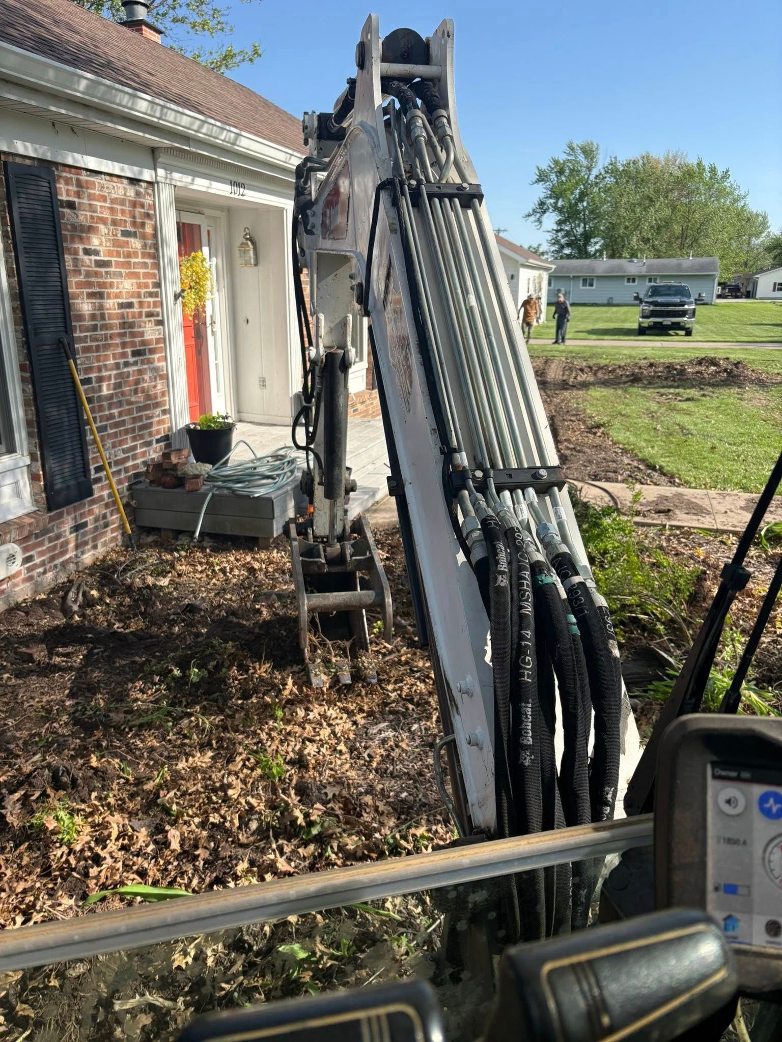 Folded black hydraulic boom lift beside a house, with hoses and metal arms leaning upright outdoors.