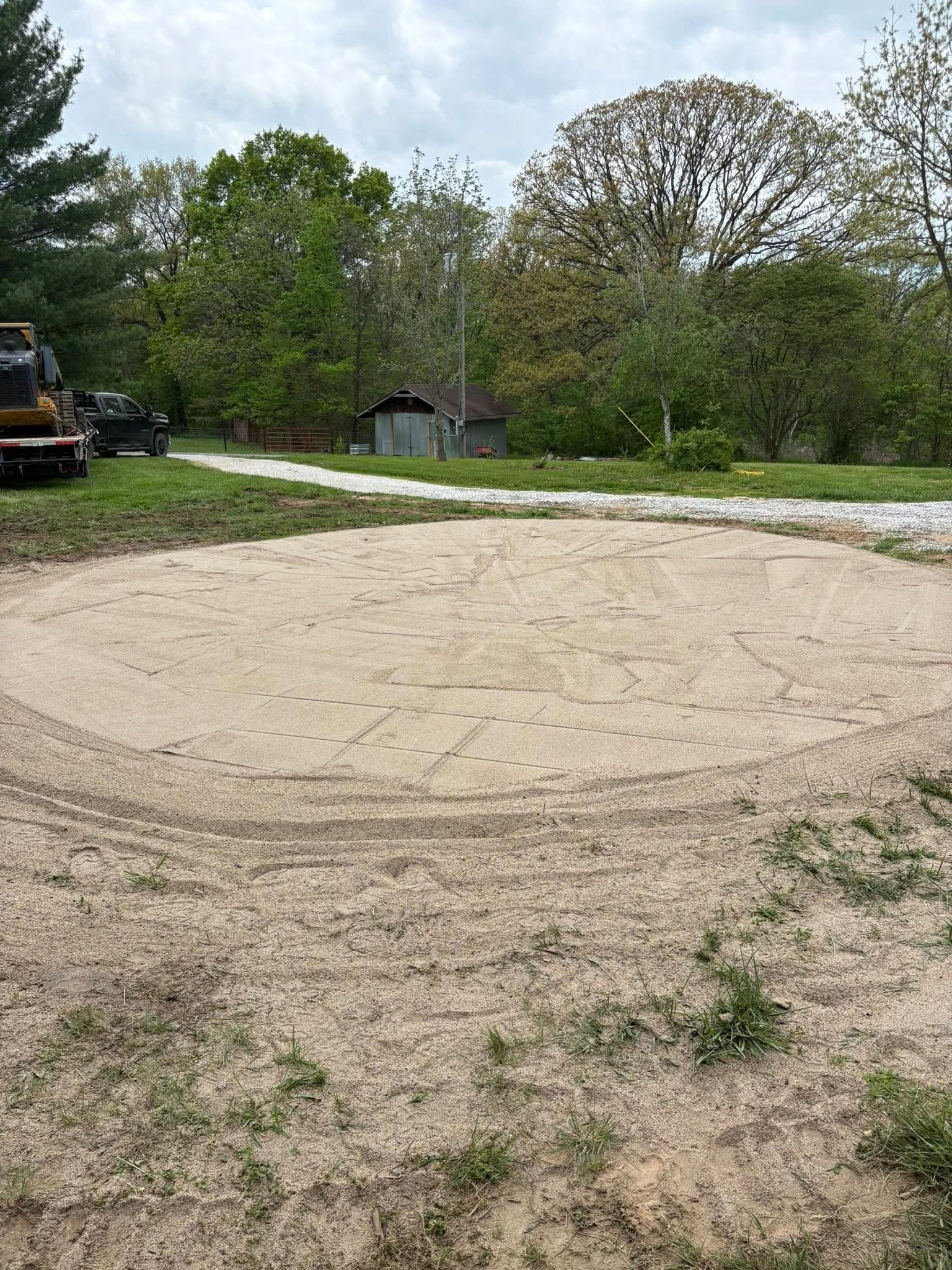 Gravel clearing beside a paved road, with trees and a parked construction vehicle in the background