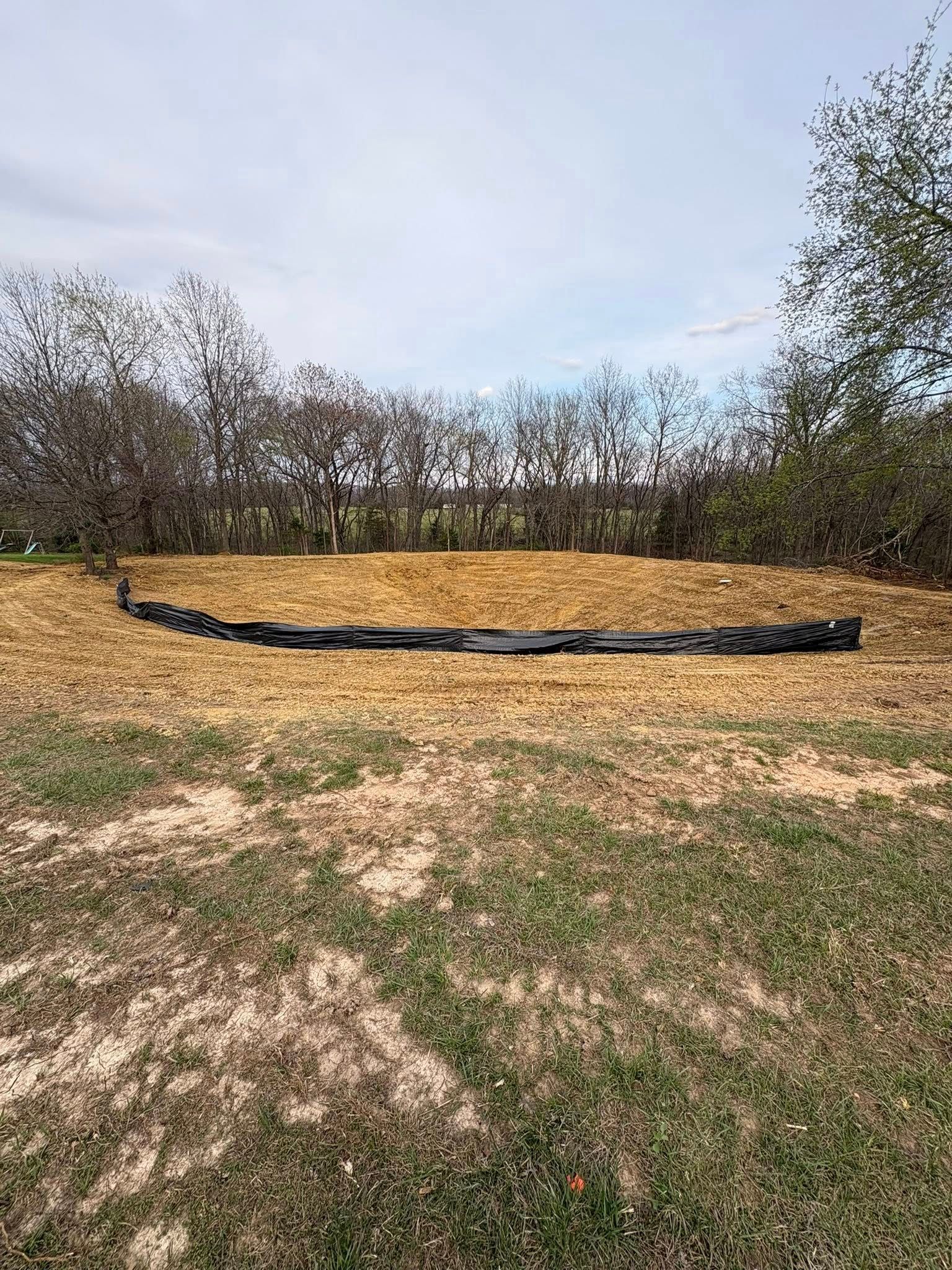 Black tarp-lined raised bed in a grassy yard with hay and trees in the background