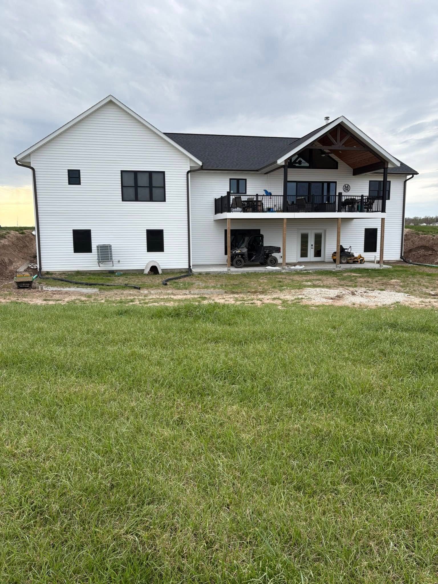 White two-story house with a balcony and damaged roof above a grassy yard.