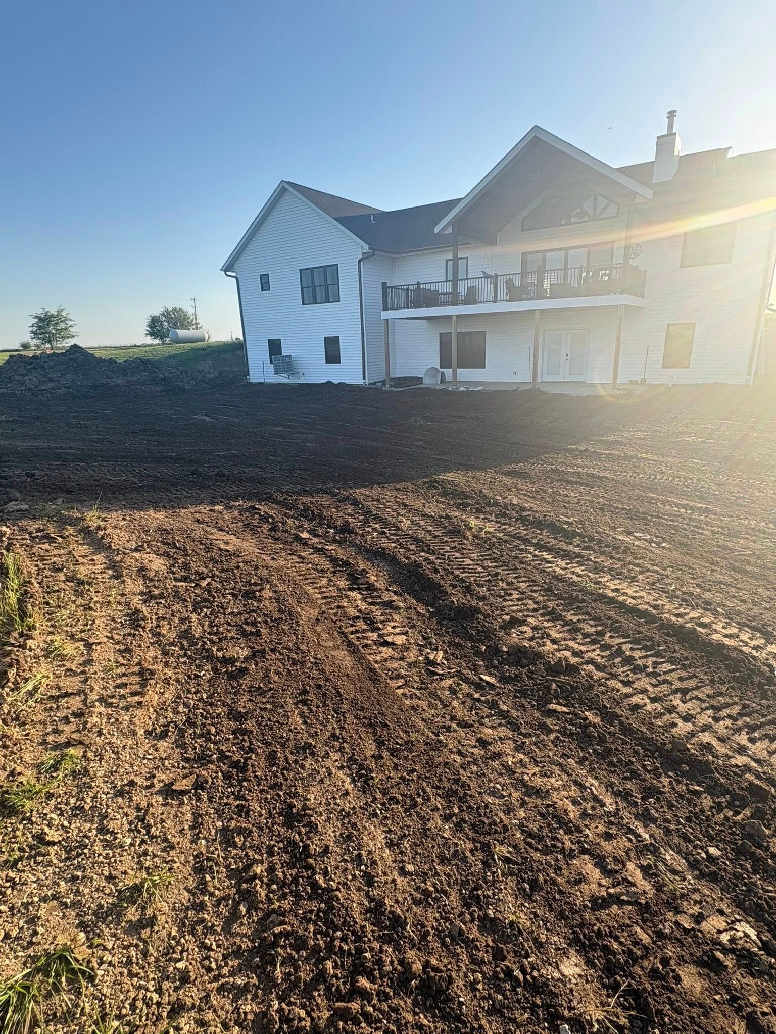 Partially built white house beside a muddy dirt lot in bright sunlight