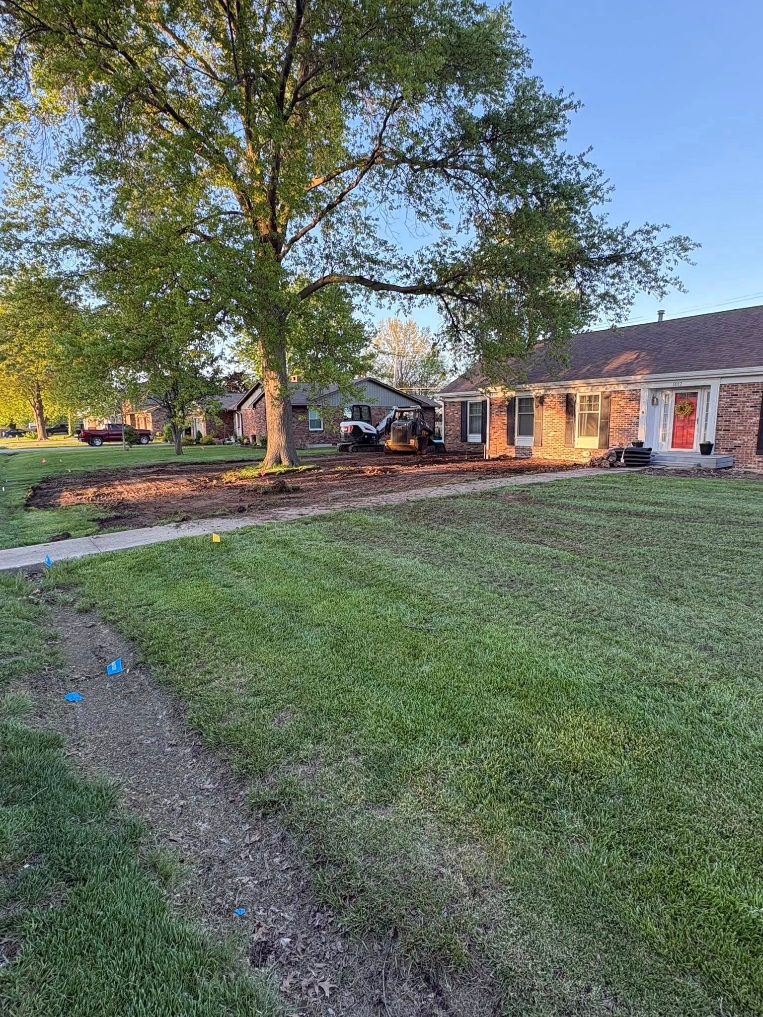 Front yard with a large tree, gravel path, and a brick house at sunset.