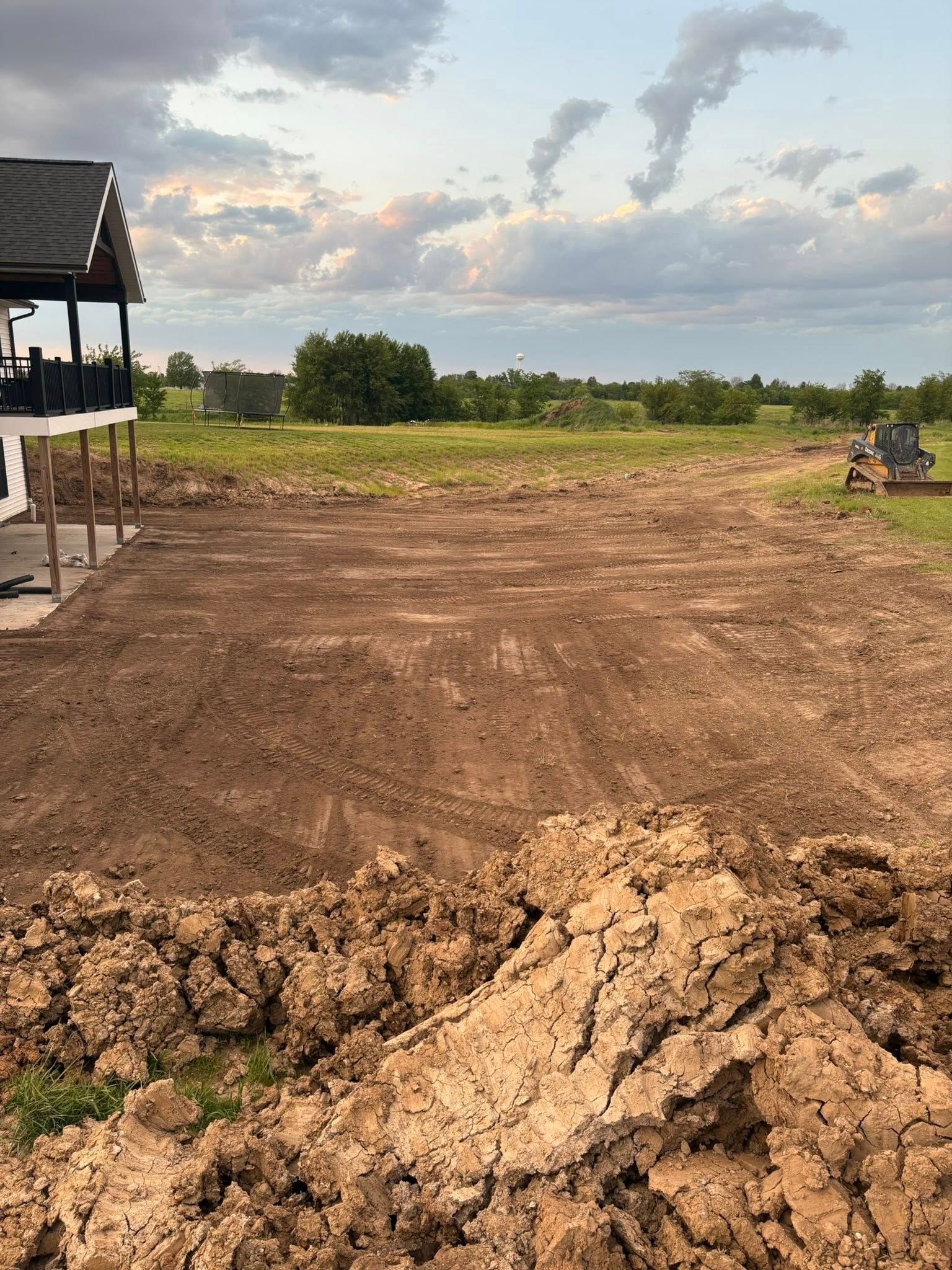 Freshly plowed dirt field beside a small shelter, with open farmland and cloudy evening sky in the background