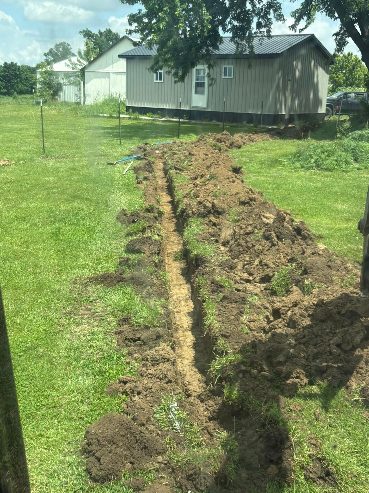 Fresh trench cut through a grassy yard toward a small white house in the background