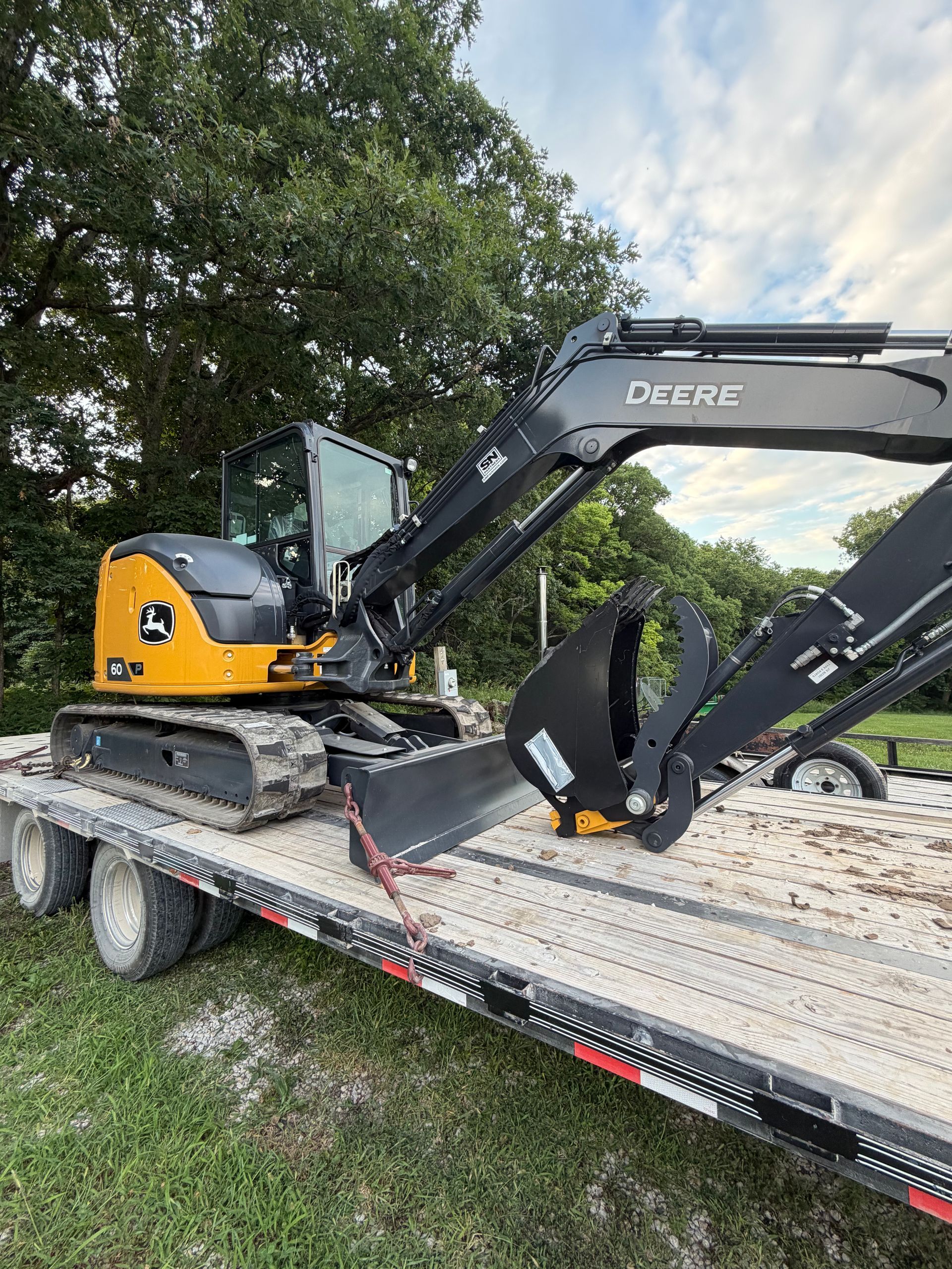 Yellow and black excavator on a flatbed trailer outdoors near trees and grass