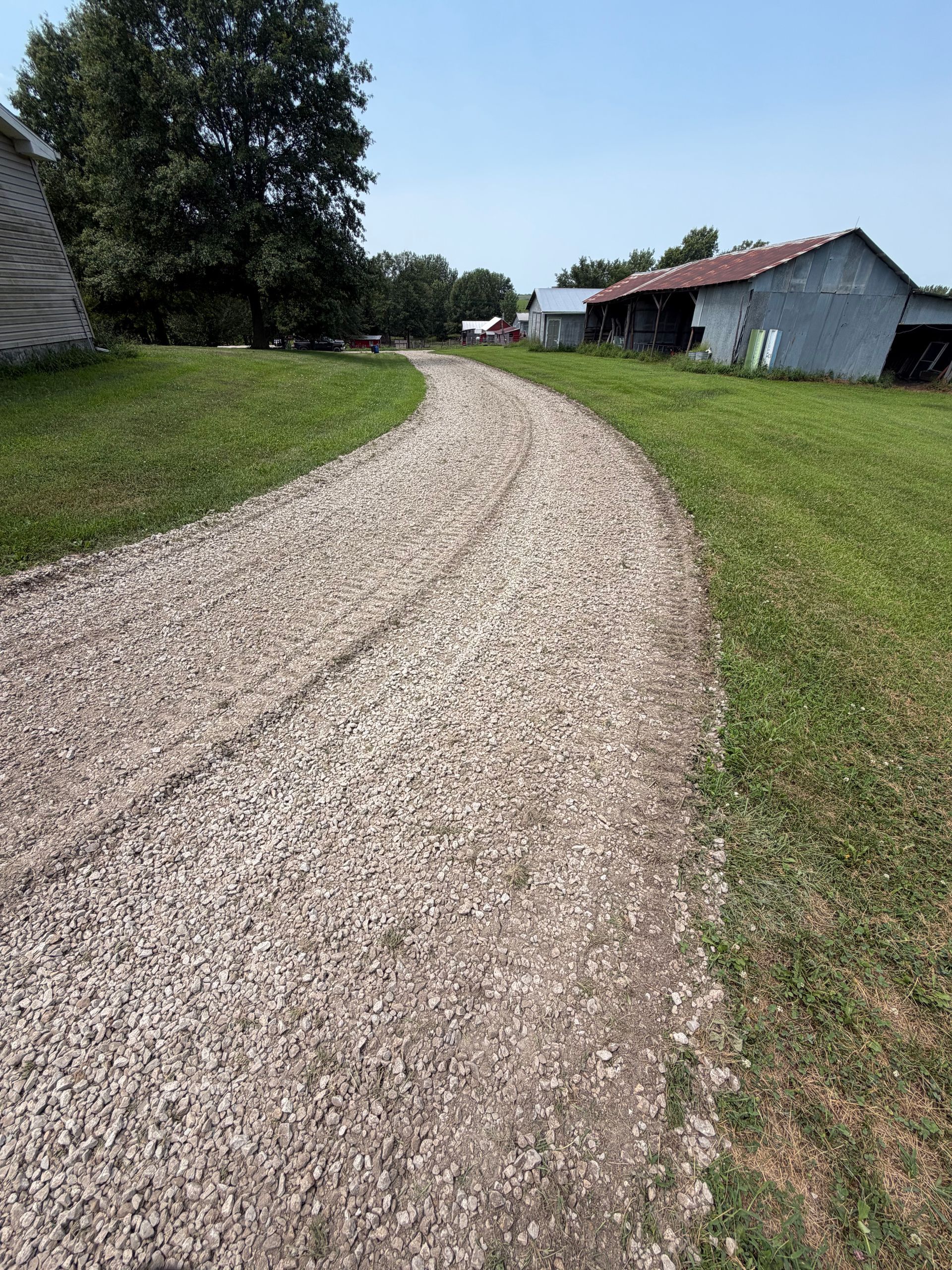 Gravel path curving through a grassy field toward buildings on a sunny day