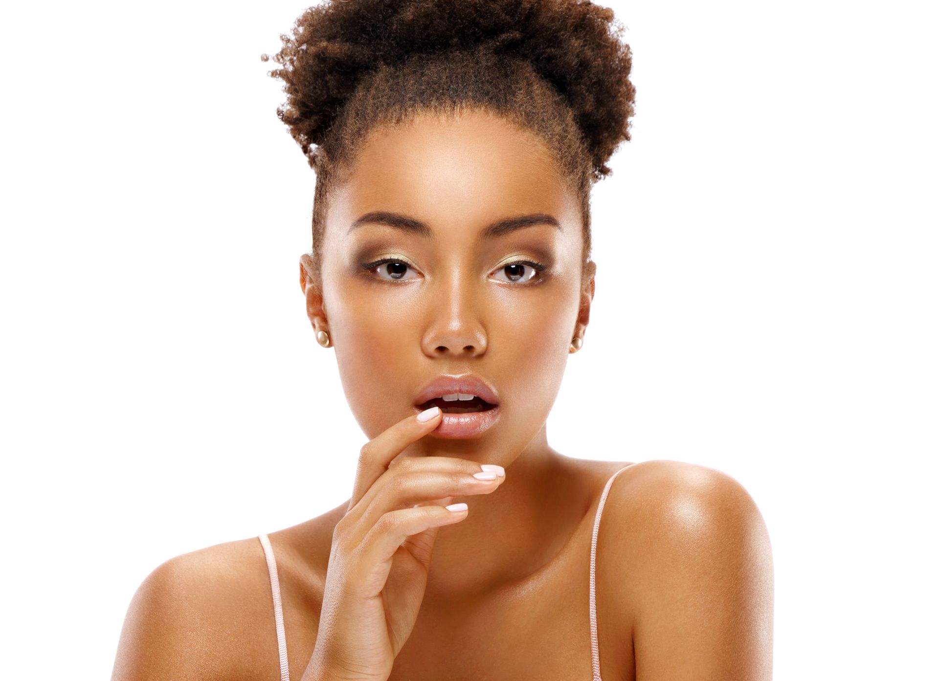 Woman with curly hair in a bun, hand on her lips, looking at the camera. White background.