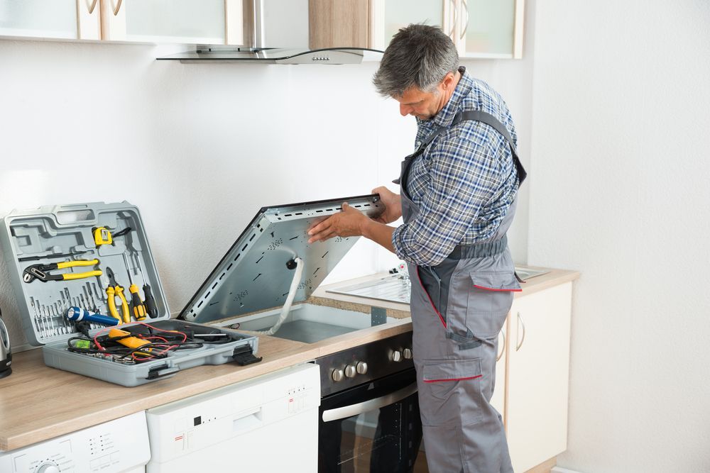 A Man is Fixing a Stove in a Kitchen — Patrick Lunney Home Appliance Service & Repairs in Maudsland, QLD