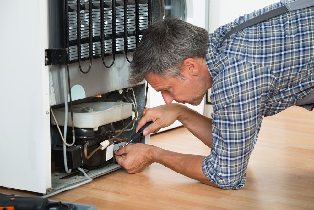 A Man is Kneeling on the Floor Fixing a Refrigerator — Patrick Lunney Home Appliance Service & Repairs in Maudsland, QLD