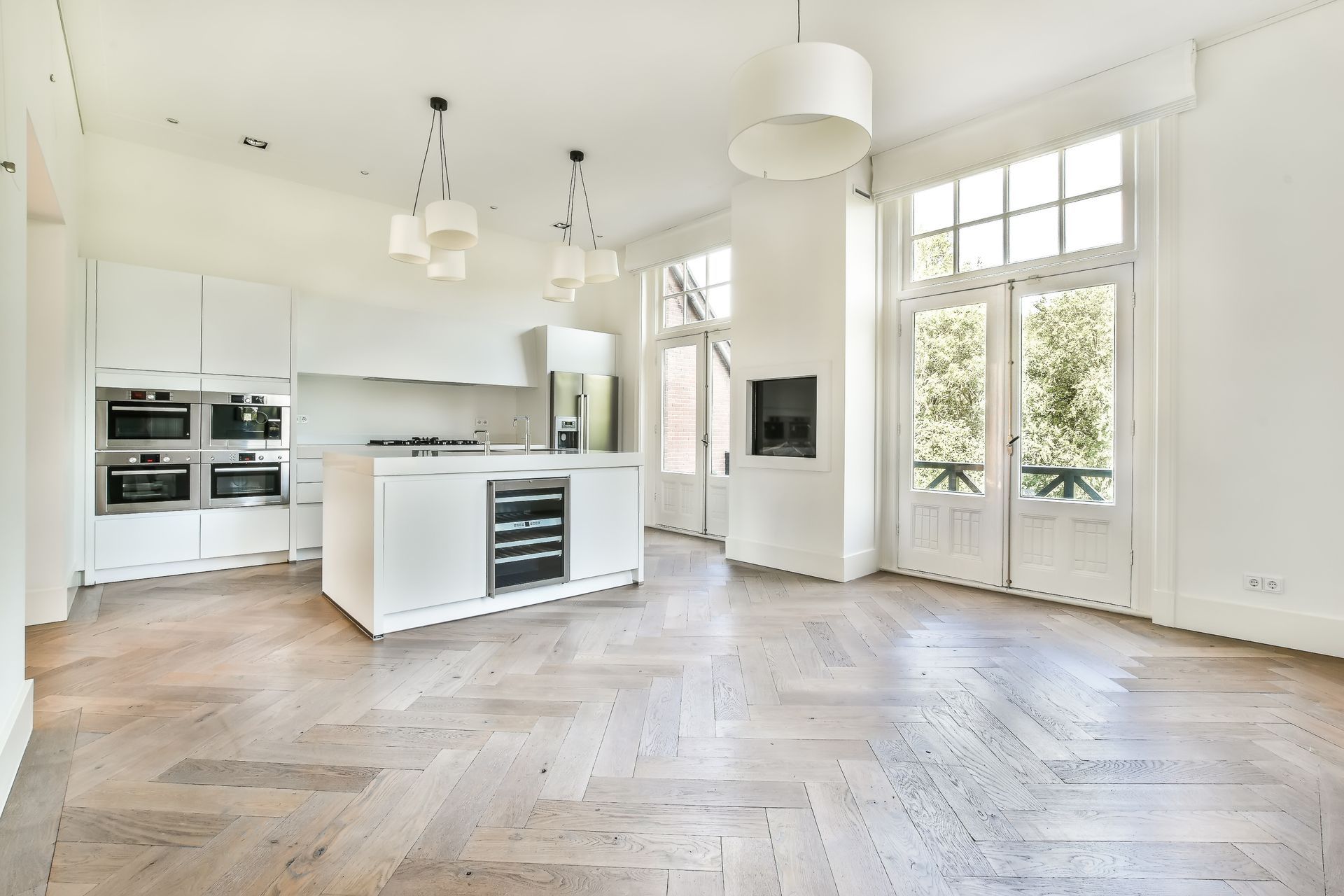 A large empty kitchen with a wooden floor and white cabinets.