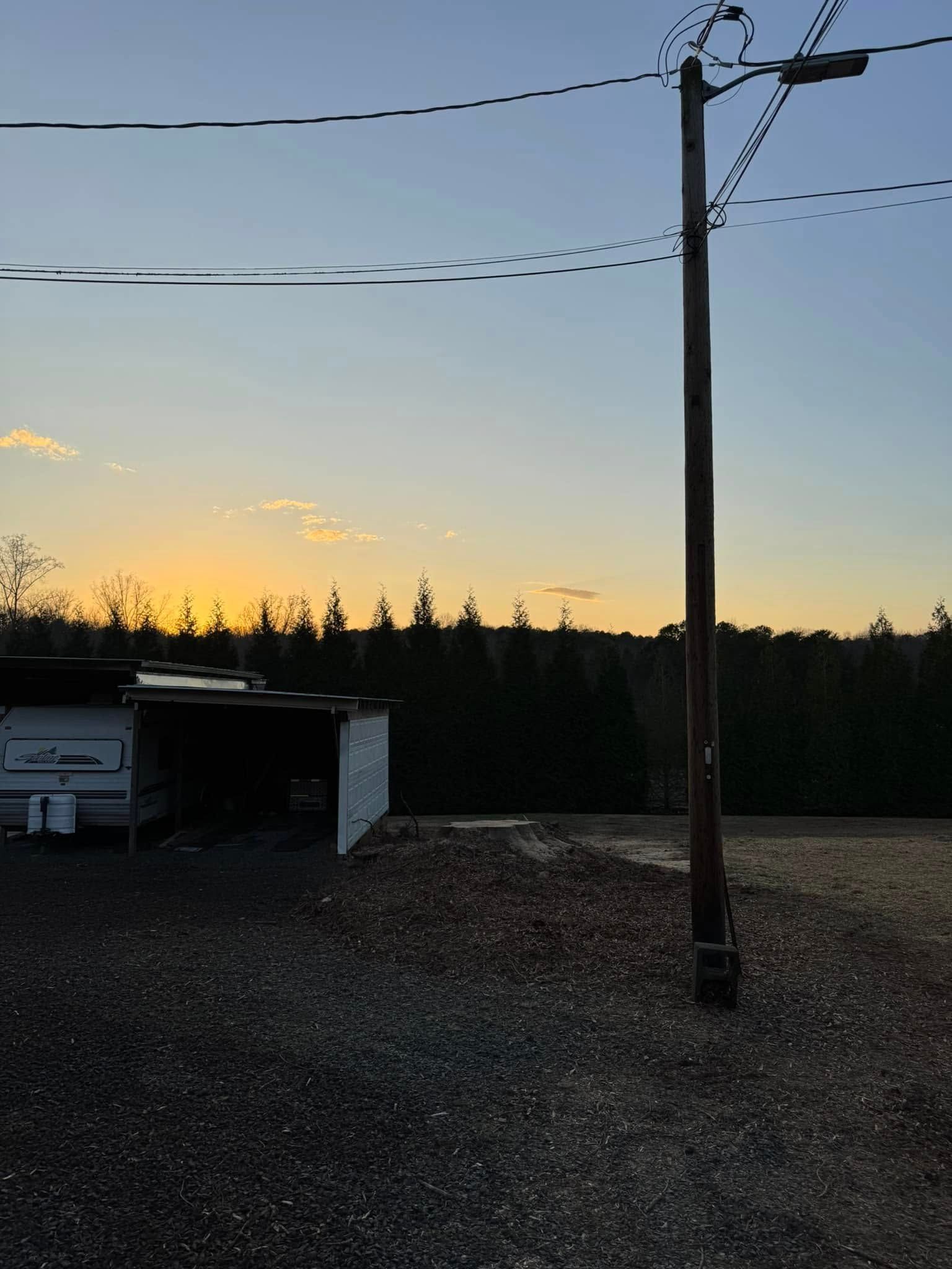 Sunset over trees, telephone pole in foreground, gravel ground.