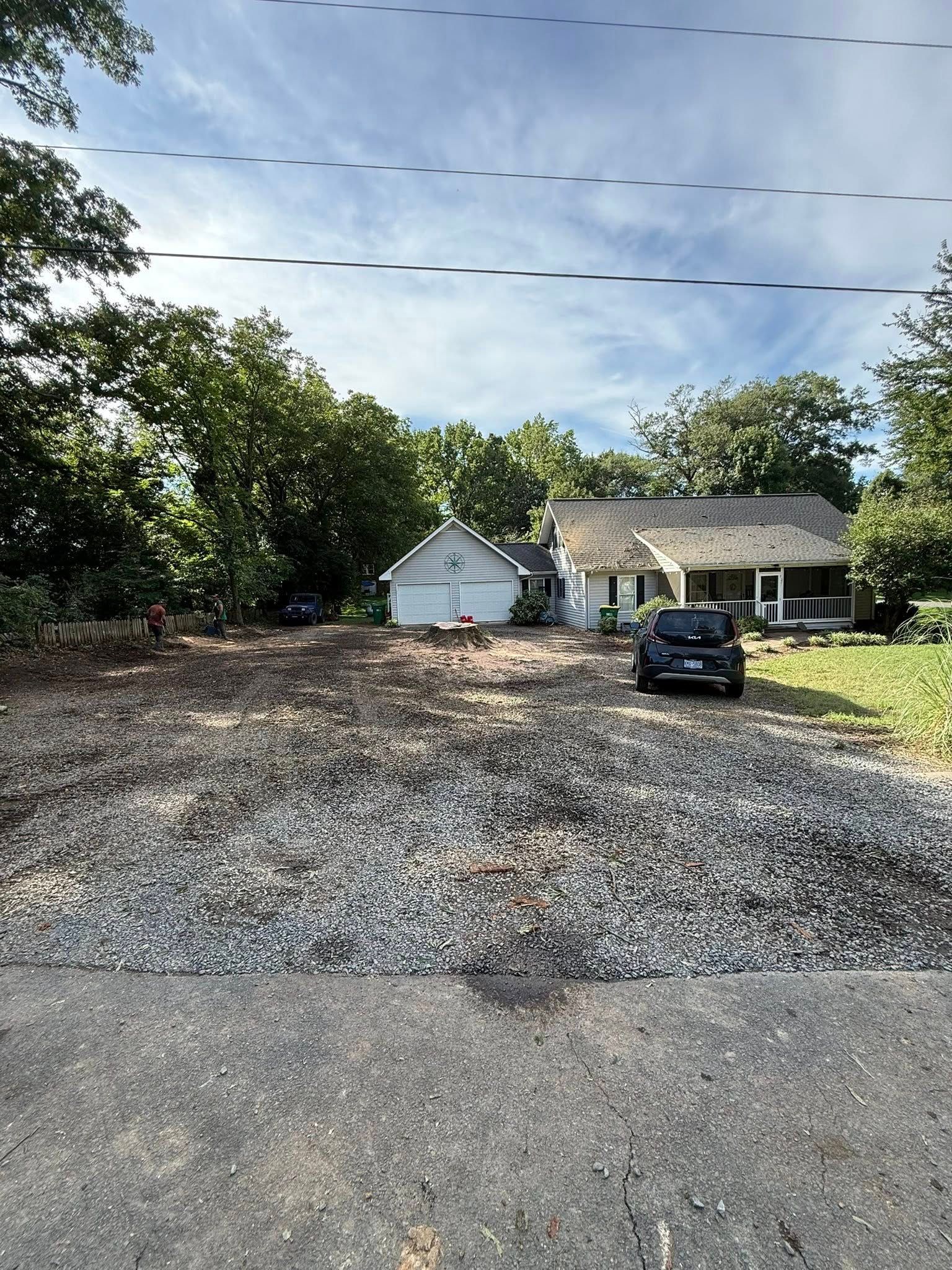 Cleared lot in front of a house, covered in gravel. A vehicle is parked in front of the house.