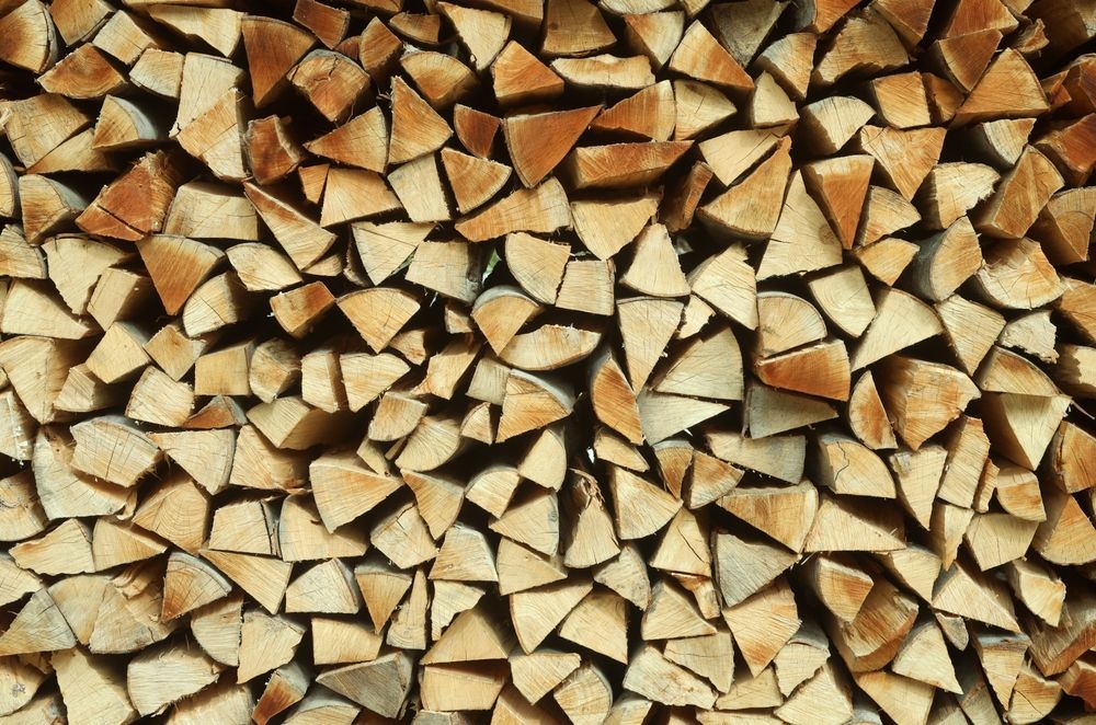 Pile of split firewood, various light brown shades, neatly stacked, filling the frame.