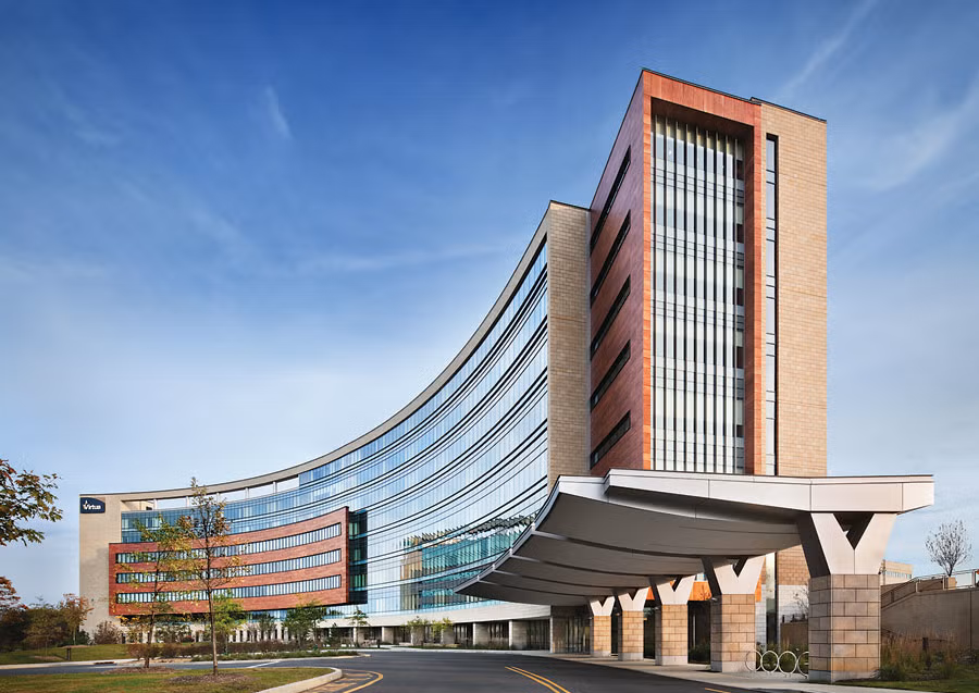 Modern hospital building with curved glass facade and covered entrance under a blue sky