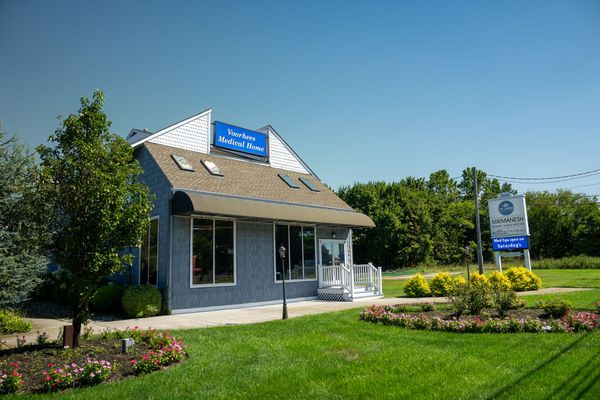Small gray building with a blue sign, landscaped flower beds, and a bright green lawn under a clear sky