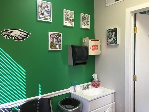 A restroom painted green with Philadelphia Eagles decor, a white sink, paper towel dispenser, and a trash can.