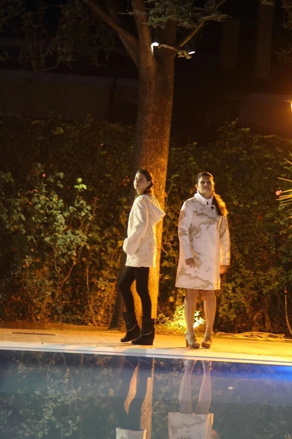 Due donne sono in piedi accanto a una piscina di notte.