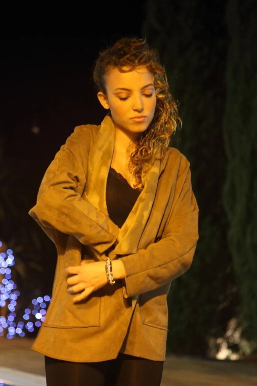 Una donna con una giacca marrone è in piedi davanti a un albero di Natale.