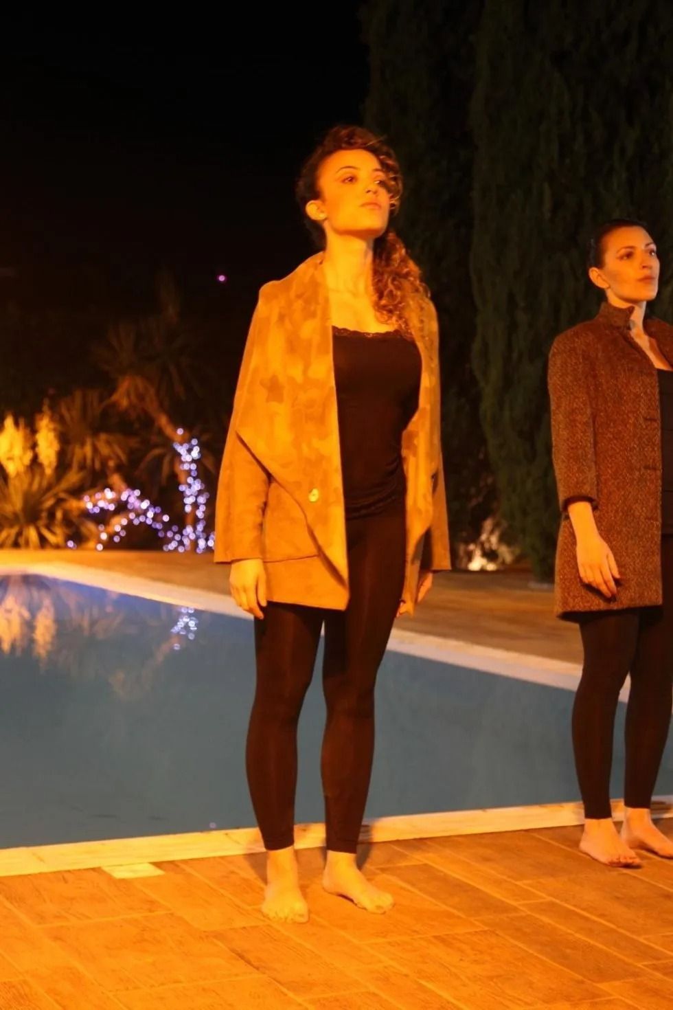 Due donne sono in piedi accanto a una piscina di notte.