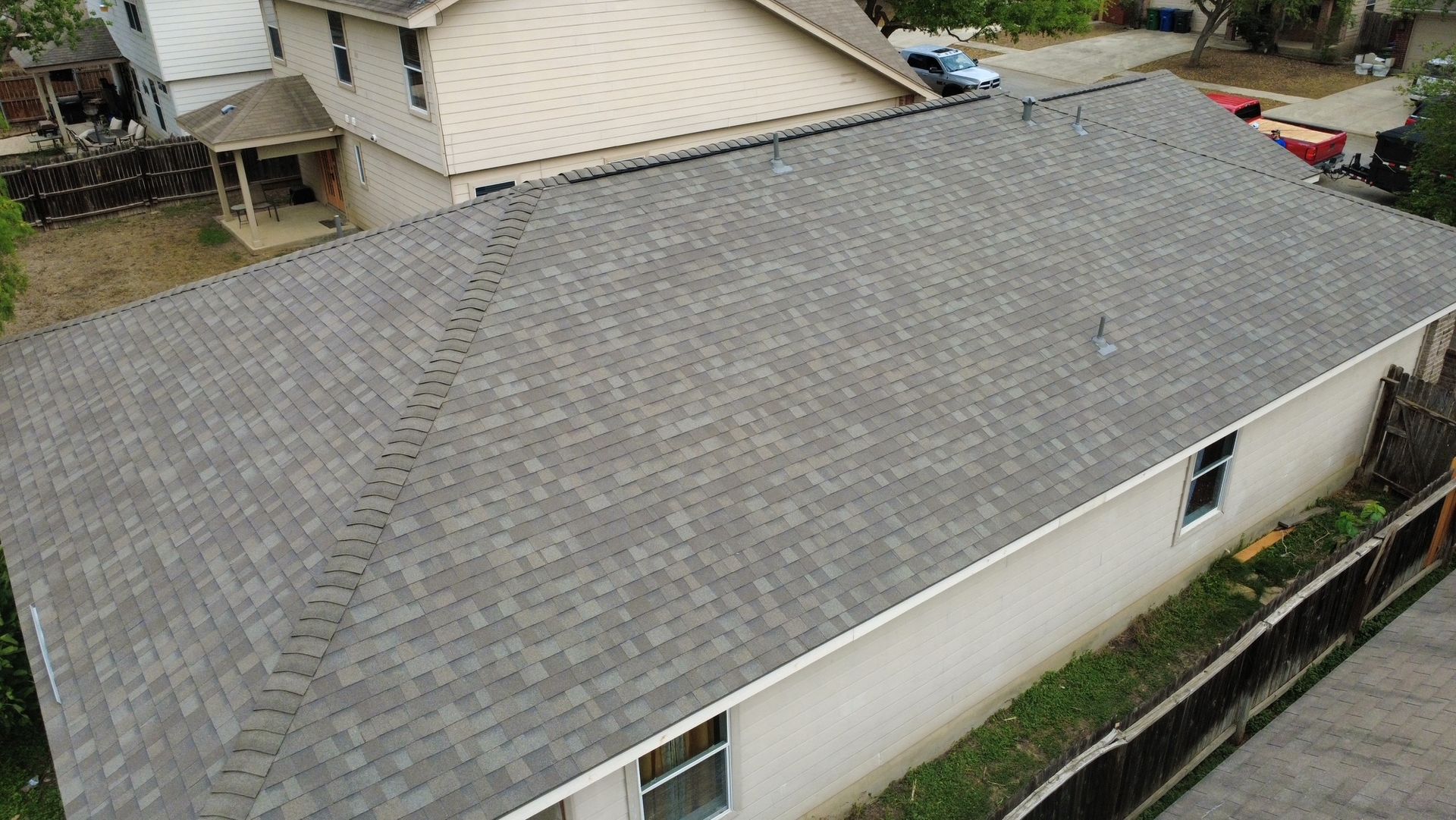 Aerial view of a gray shingled house roof with neighboring homes visible nearby.