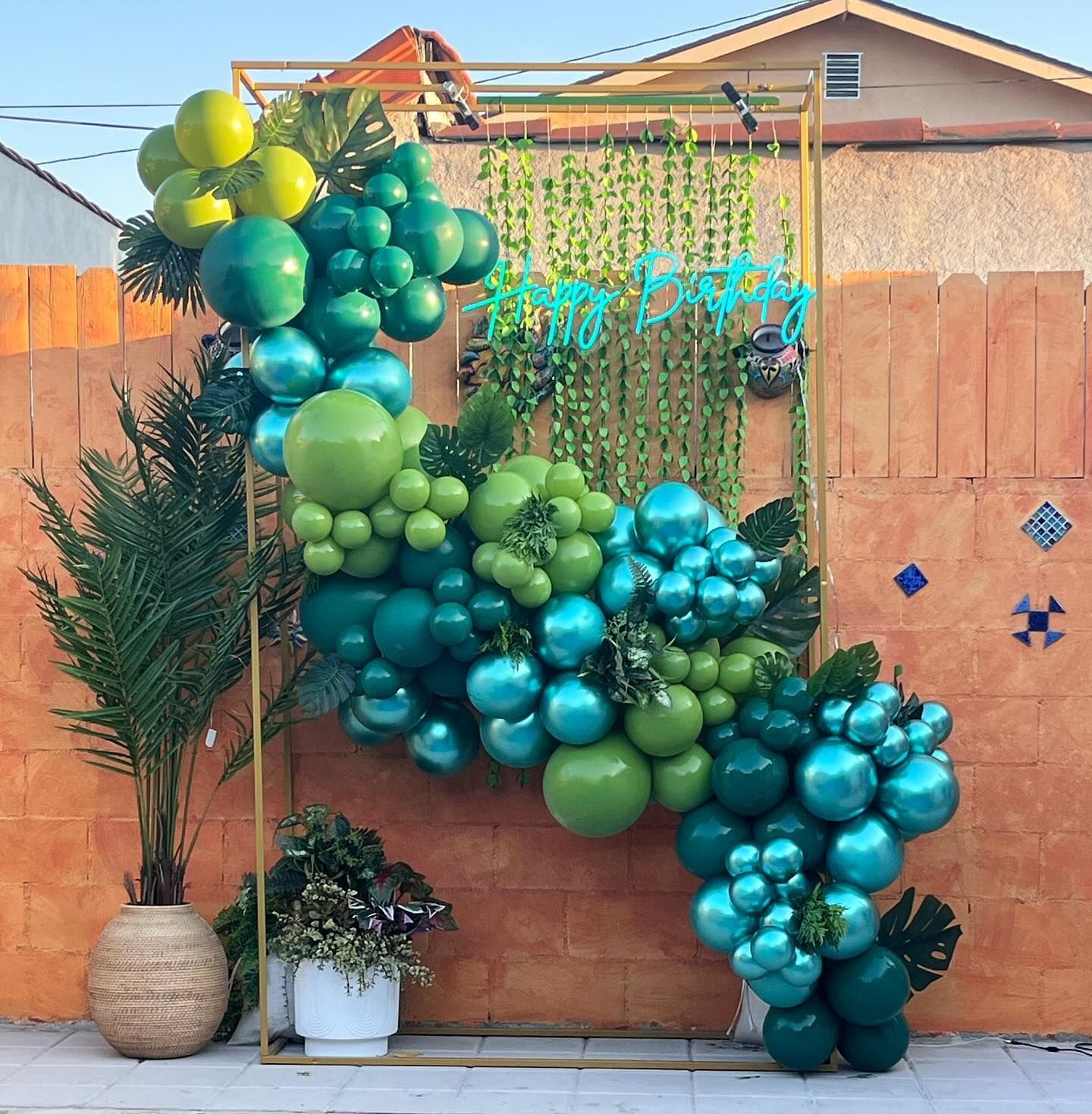 a bunch of green and blue balloons are hanging from a metal frame