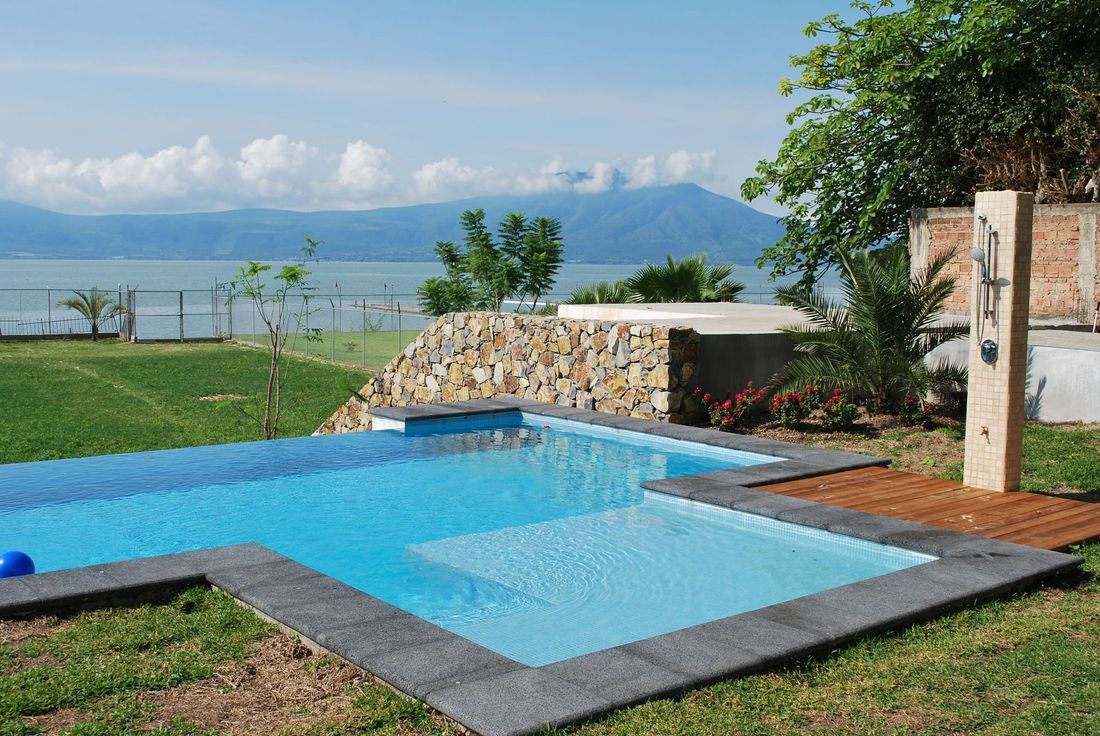 Swimming pool overlooking a lake, with mountain in the background. Green grass and blue sky.