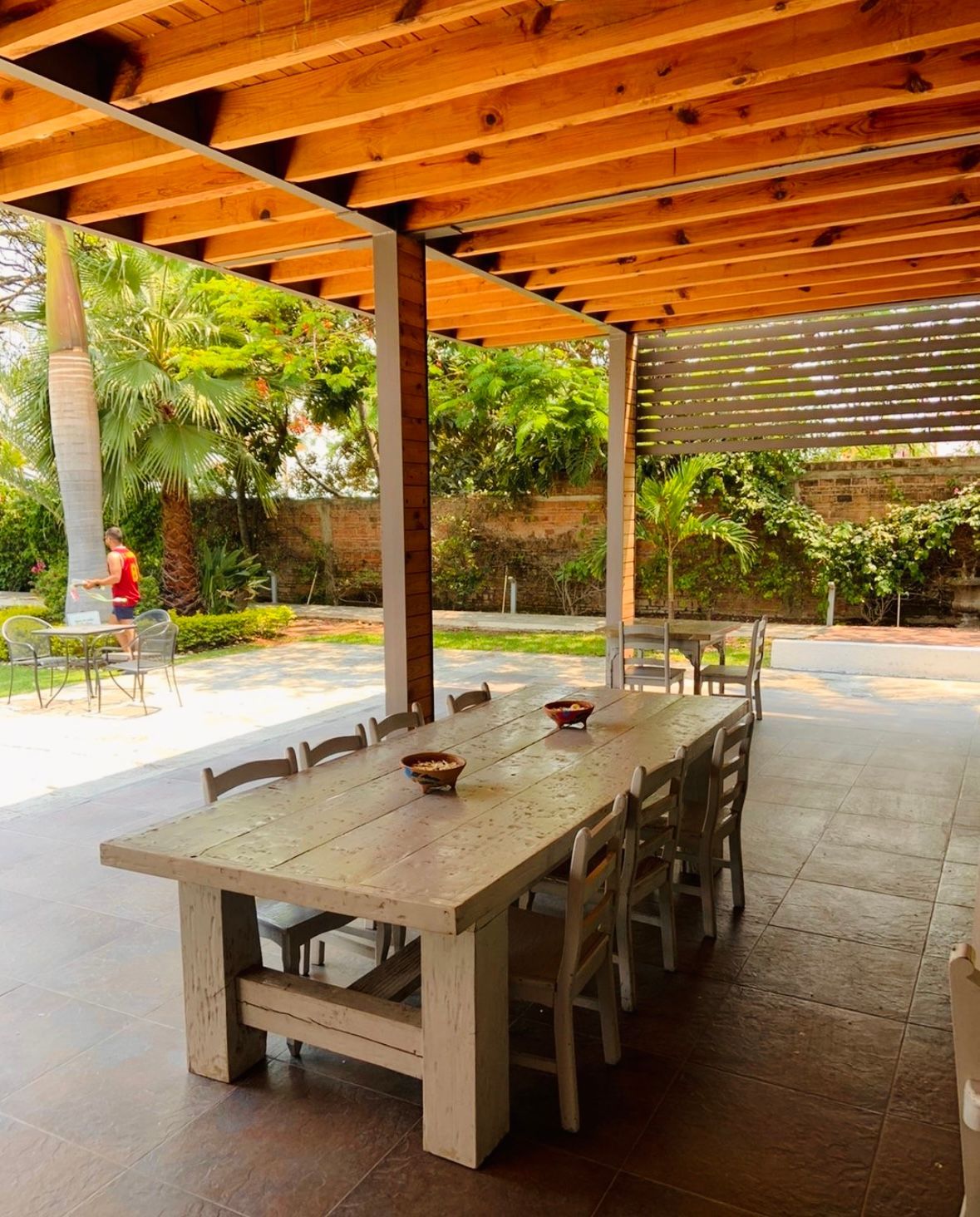 Outdoor dining area with a long wooden table, chairs, and a wood beam pergola.