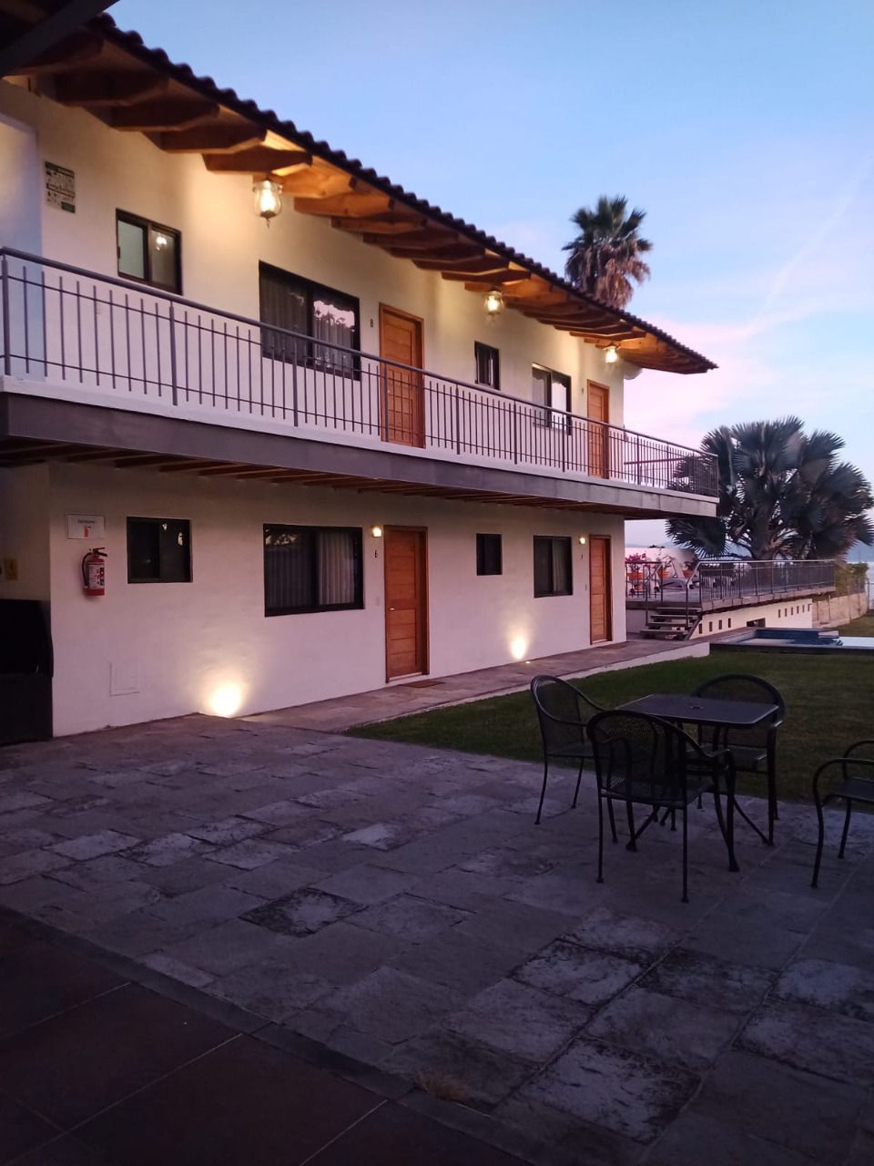 Two-story building with balconies, exterior lighting, patio furniture, and a grassy area.