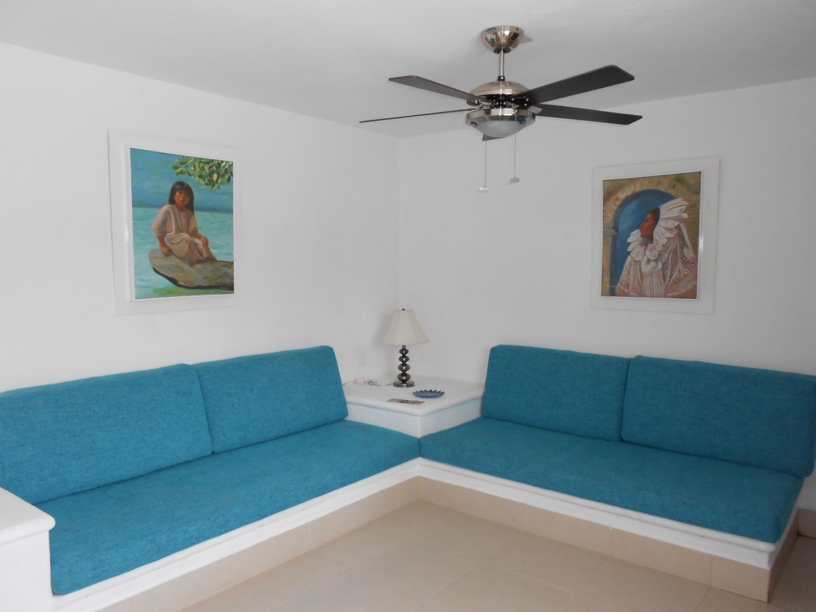 A bright room with blue sofas, art on the walls, and a ceiling fan.