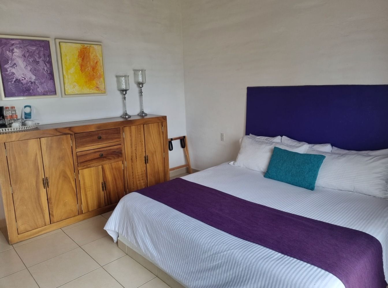 Bedroom with a bed, dresser, art, and decorative candles. Purple and gold accents.