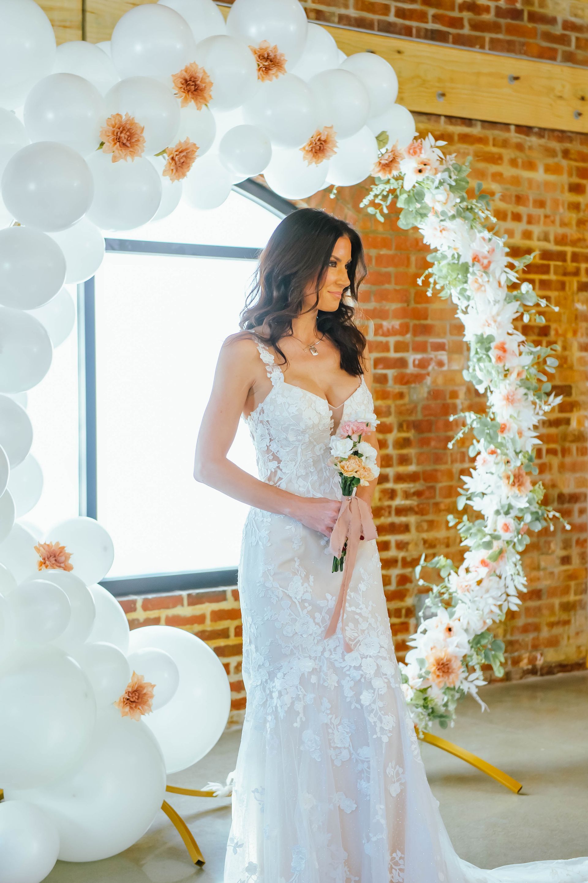 A bride in a wedding dress is standing in front of a balloon arch.