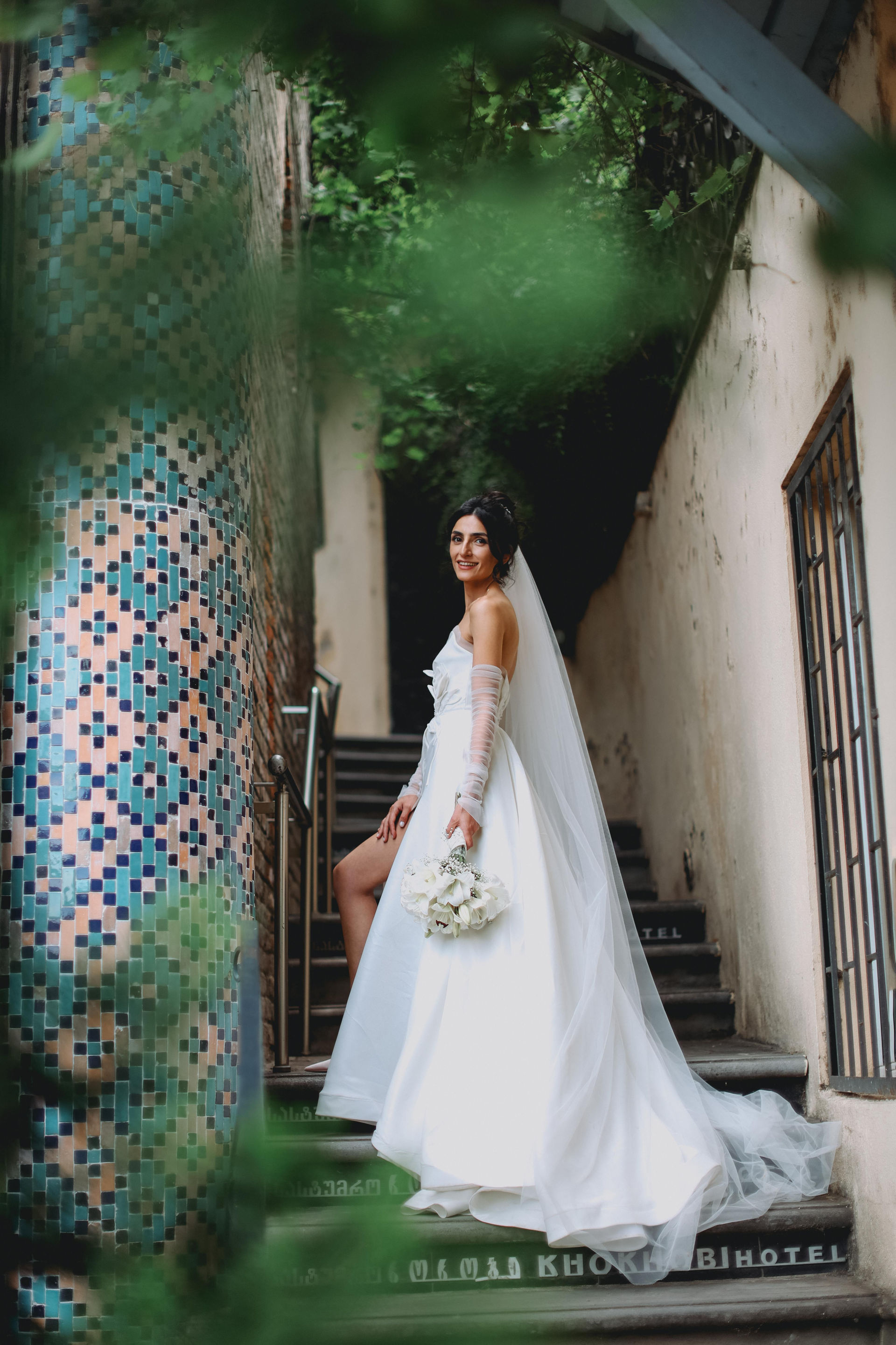 A bride in a wedding dress is standing on a set of stairs holding a bouquet of flowers.