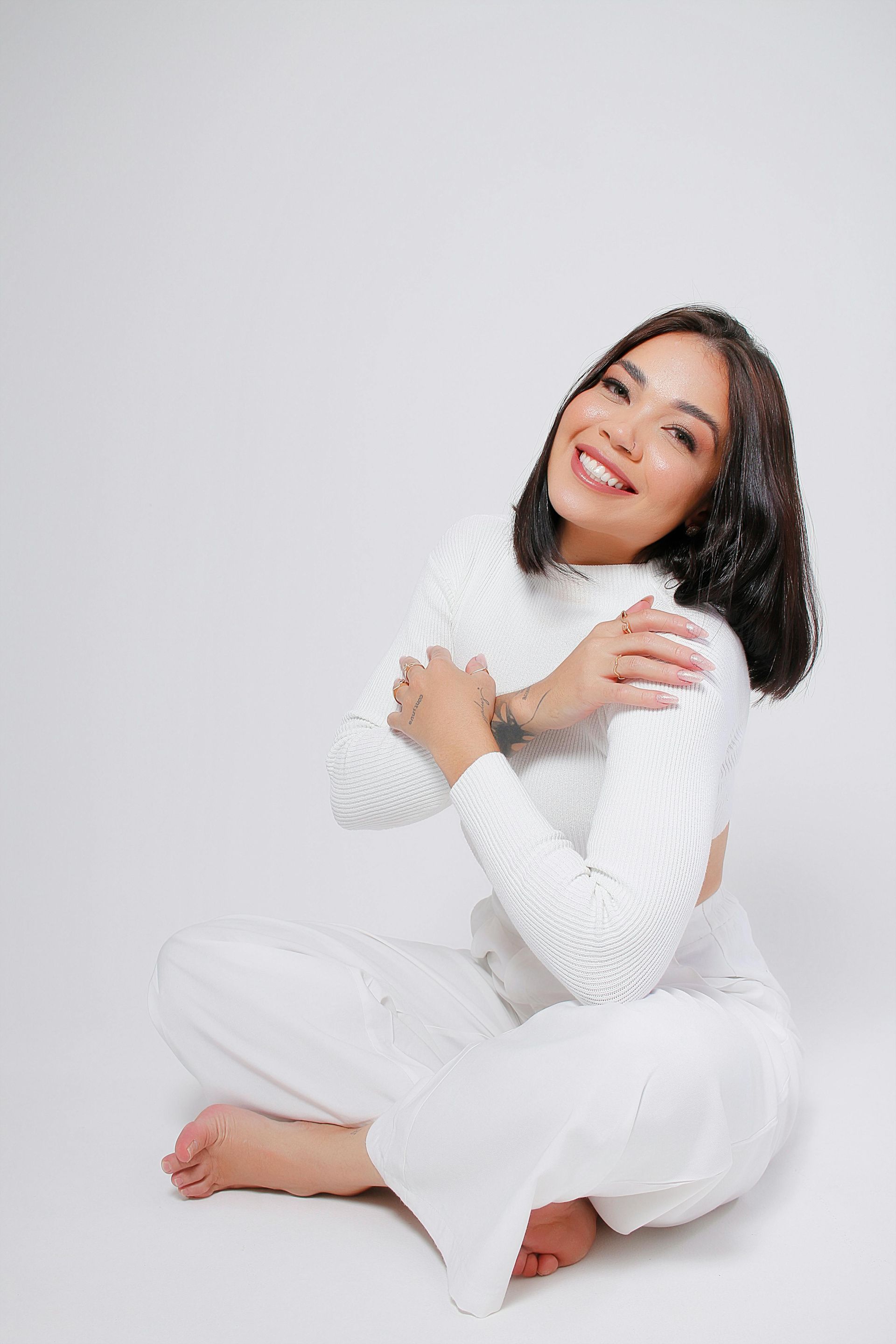 A woman is sitting on the floor with her legs crossed and smiling.