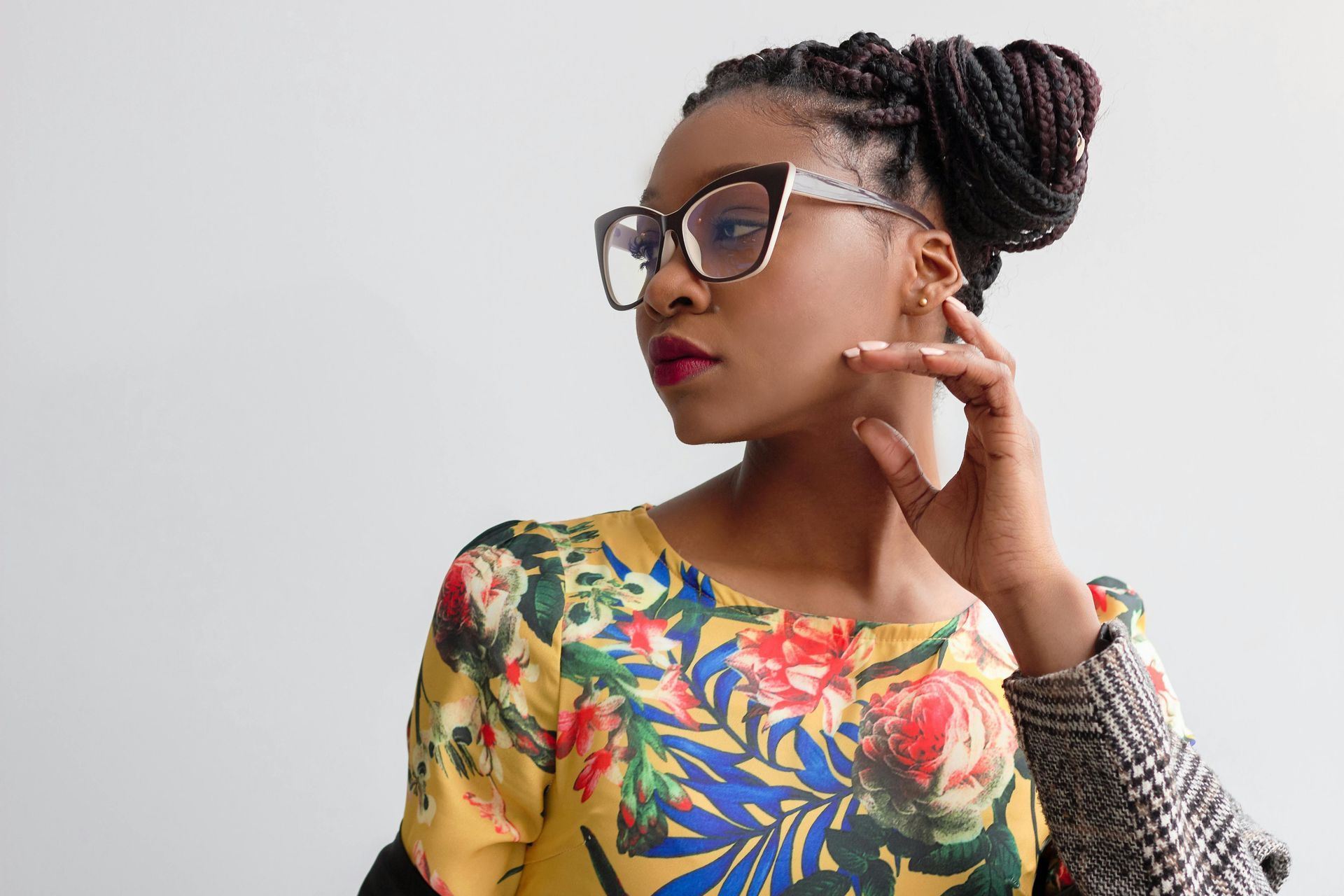 A woman wearing glasses and a floral shirt is touching her face.