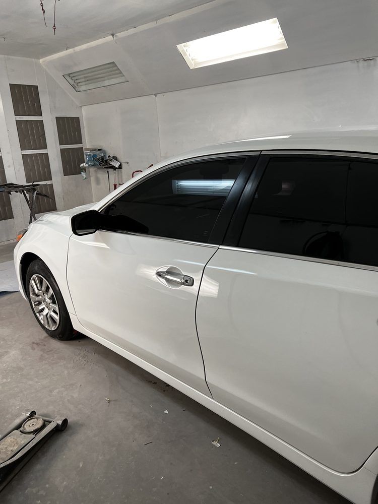 White sedan parked inside a brightly lit garage or auto body shop.
