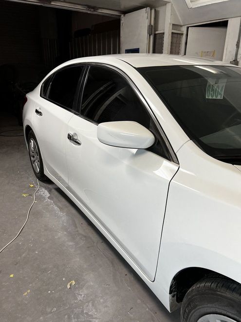 White sedan parked in a garage, side view with a partially visible front wheel and mirror.