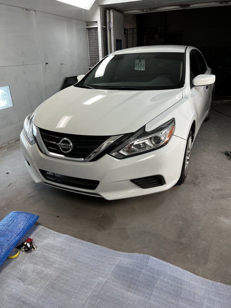 White Nissan sedan parked indoors in a gray garage or workshop