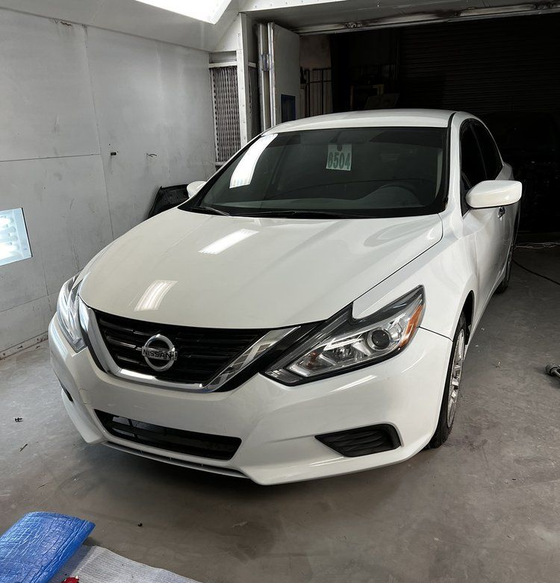 White Nissan sedan parked in a garage, viewed from the front-left angle.