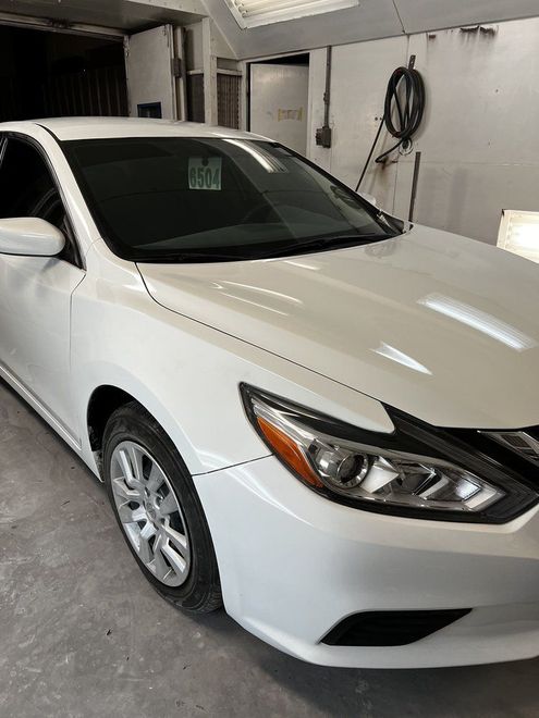 White sedan parked in a garage, front three-quarter view