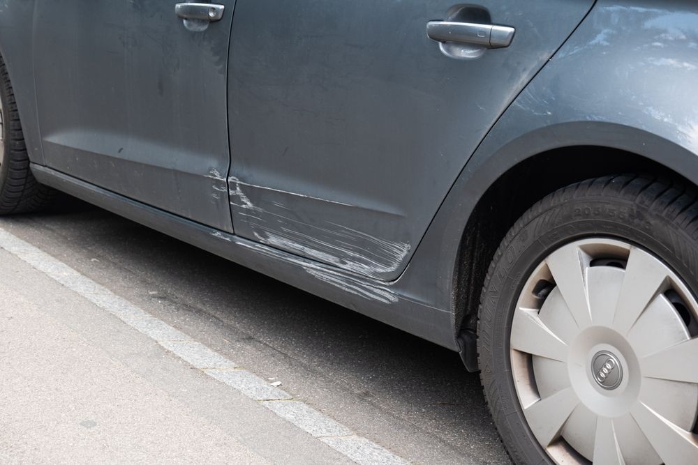 Gray car with side-door and lower-panel scrape damage near the rear wheel