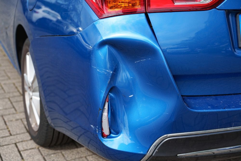 Blue car’s rear bumper dented and scratched near the taillight on a brick driveway