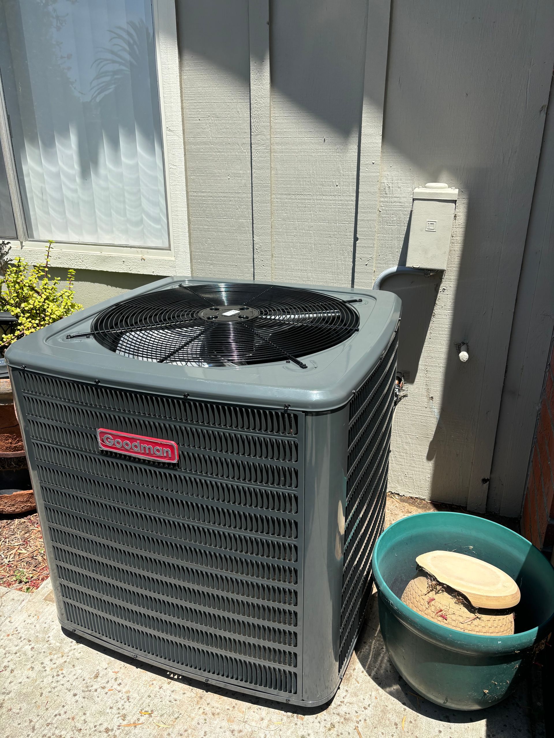 An air conditioner is sitting on the side of a building next to a green bowl.