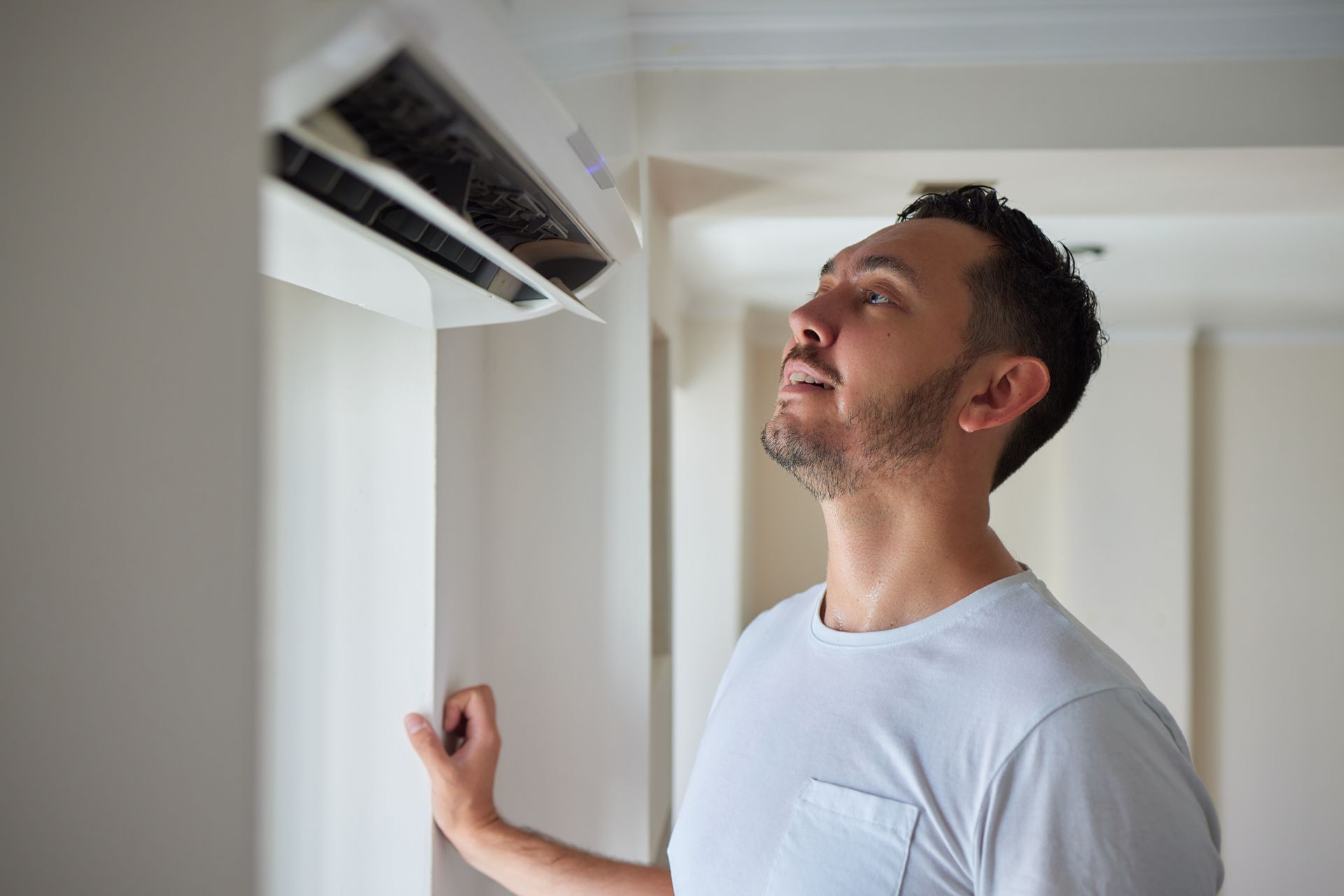 Man looking up at a wall-mounted air conditioner indoors.