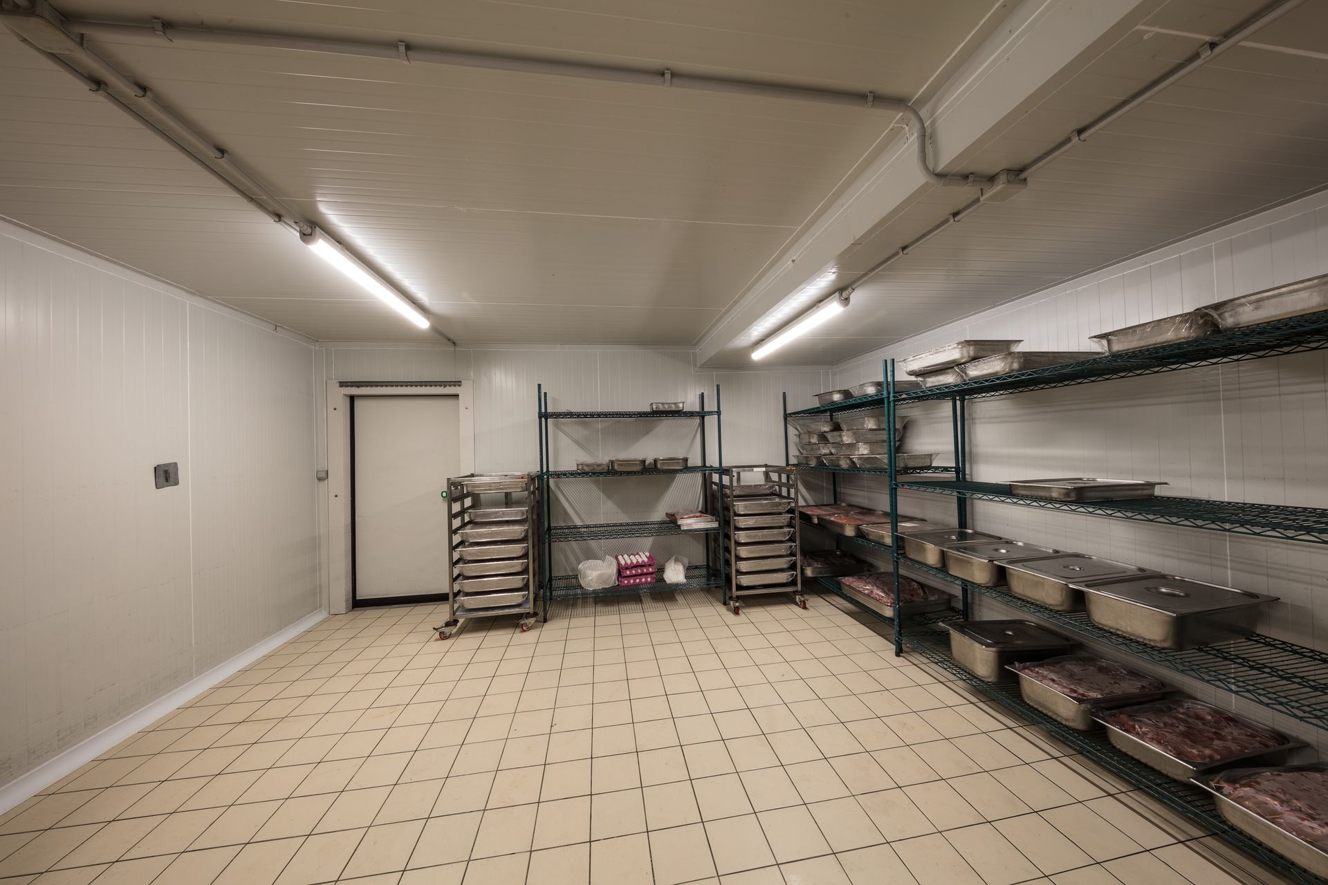 Empty storage room with metal shelves, stacked bins, and tiled floor under fluorescent lights