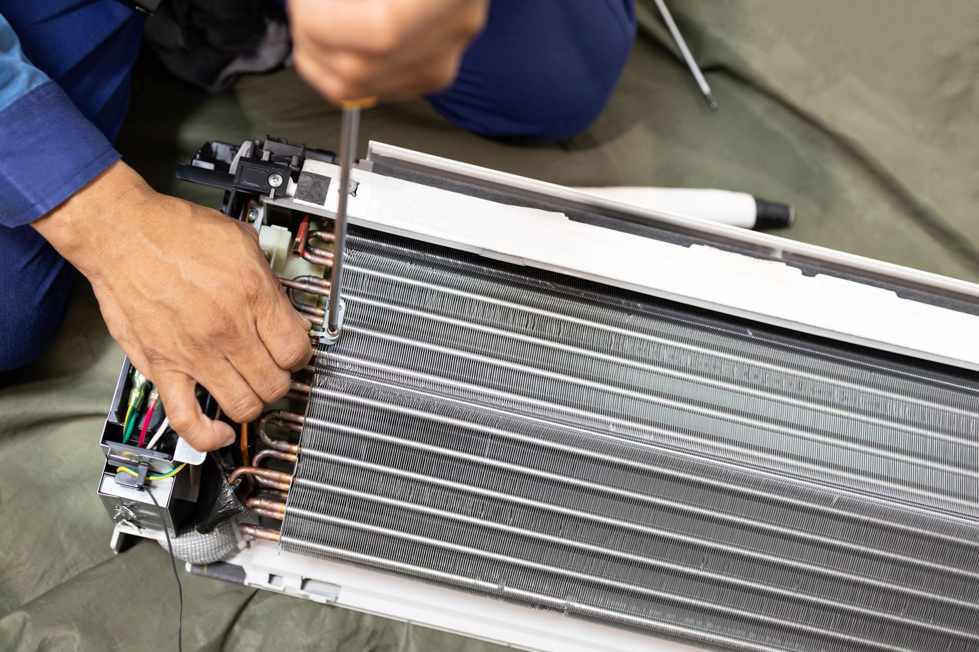 Person working on a metal radiator or heat exchanger with a wrench and copper tubes exposed