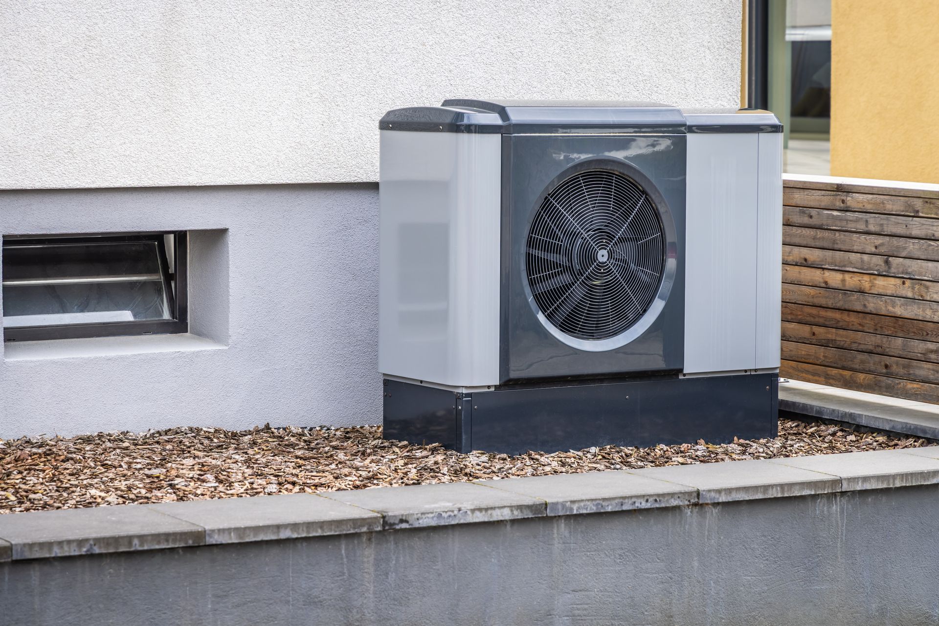 Outdoor heat pump unit beside a building wall and stone planter edge