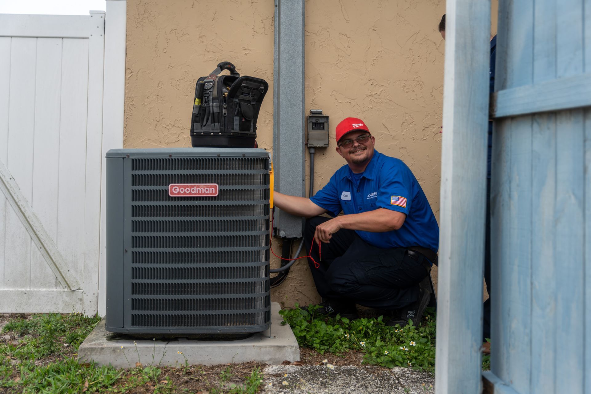 A man is kneeling down next to an air conditioner.