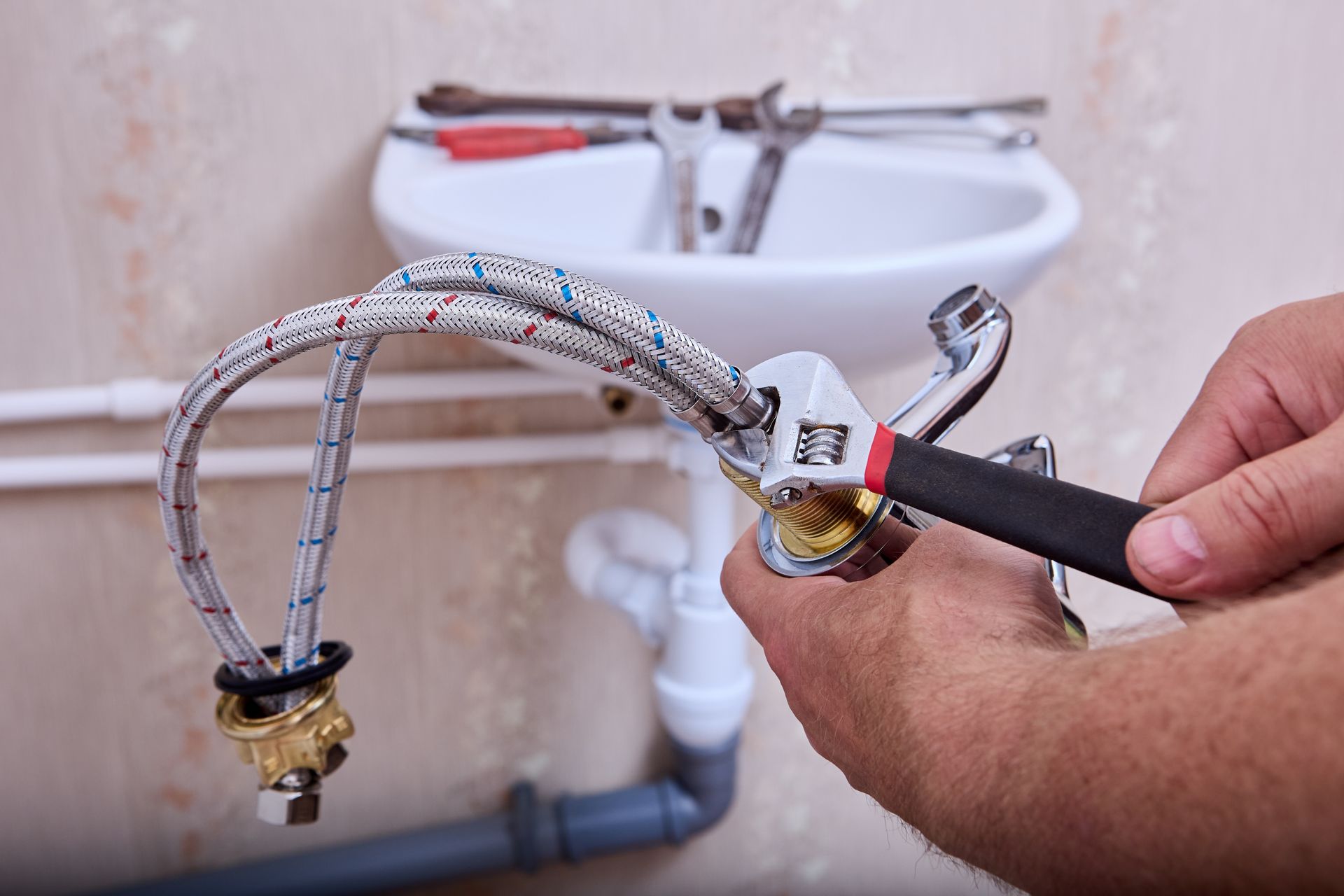 Plumber using a wrench to tighten a hose connection under a bathroom sink.
